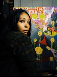 a woman sitting in front of a colorful painting